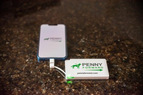 solar-powered battery bank charging an iPhone 13. The Penny Forward logo is on the screen
