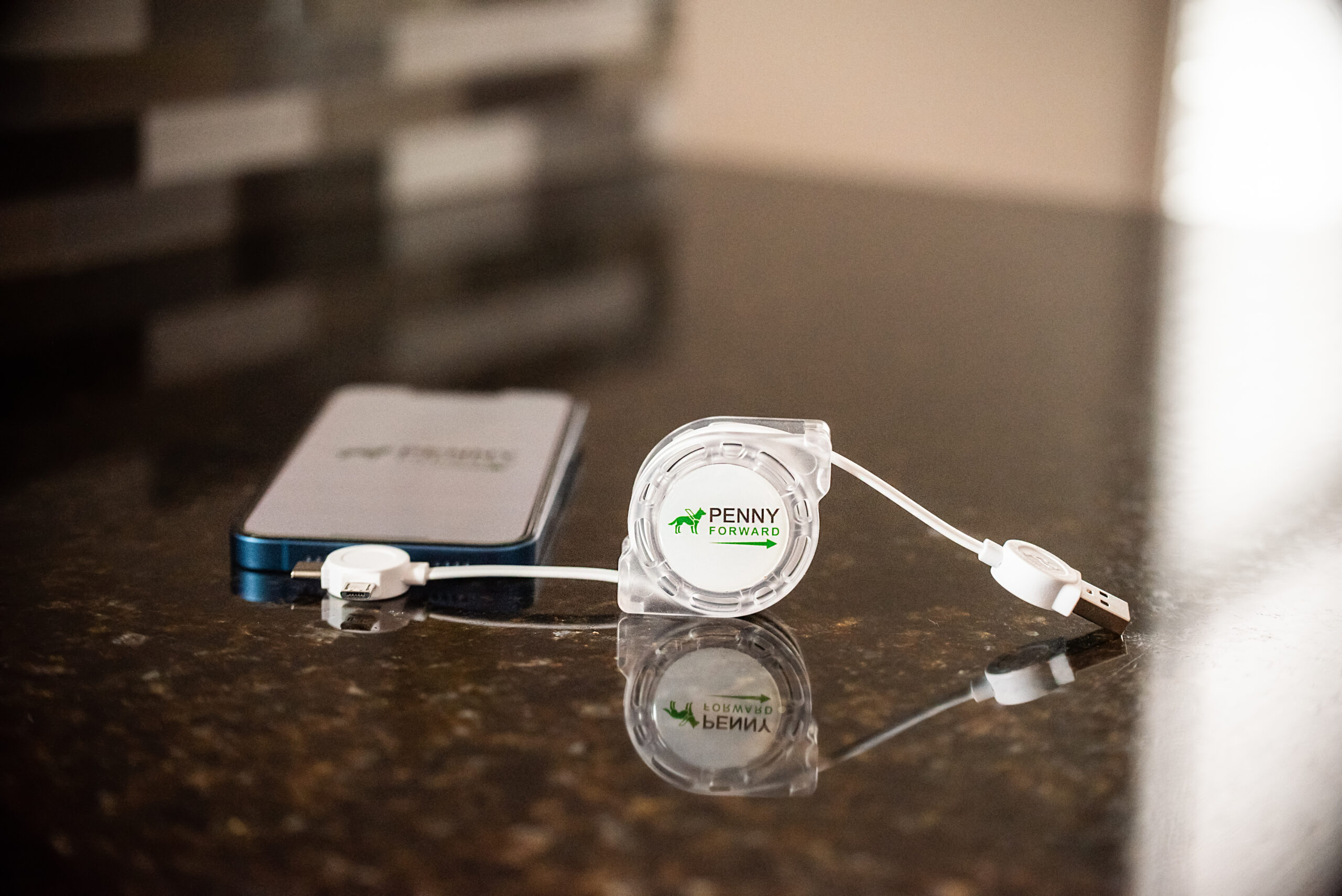 Retractable universal USB cable plugged into an iPhone 13 with the Penny Forward logo displayed on the screen