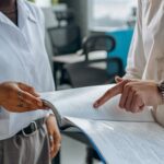Colleagues Standing in White Long Sleeve Shirts Discussing a Financial Report