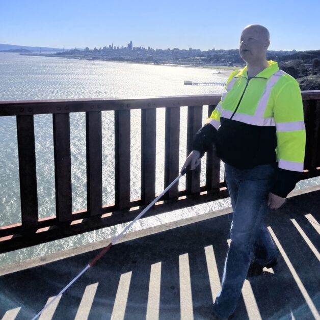 Chris Peterson walking on the Golden Gate Bridge with his new two-piece telescoping cane. The bay and city are in the background
