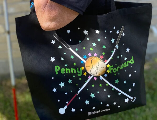 photo of Penny Forward black tote. The design has two white cane’s crossed in an x shape with a penny in the center. "Penny" is on the left of the penny with "Forward" on the right in green. There are colorful stars all around the graphic with Blind Girl Designs at the bottom.